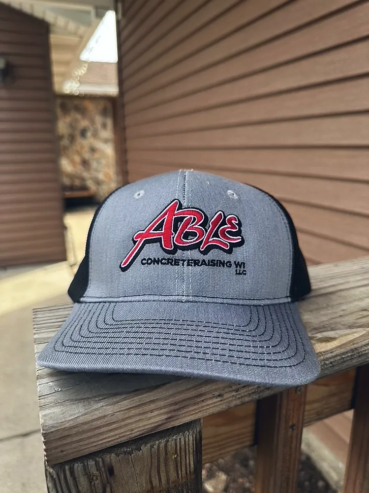 Gray and black trucker cap with raised embroidered Able Concrete Raising WI logo, custom hat embroidery in Wausau, WI