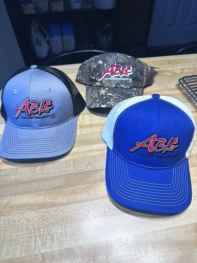 Gray, camo and royal blue trucker caps with raised embroidered Able Concrete Raising WI logo, custom hat embroidery in Wausau, WI